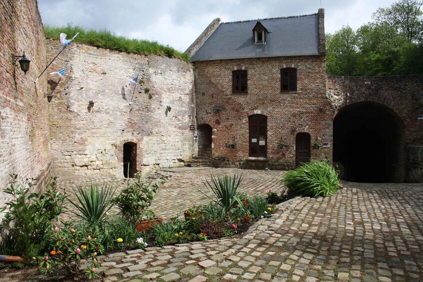 A historic courtyard with a cobblestone path, brick buildings, and a covered archway. 3