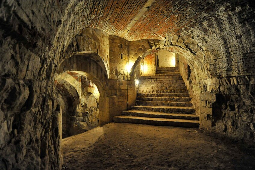 An ancient stone staircase leading upwards in a cave-like structure with arched openings and a brick ceiling. 5