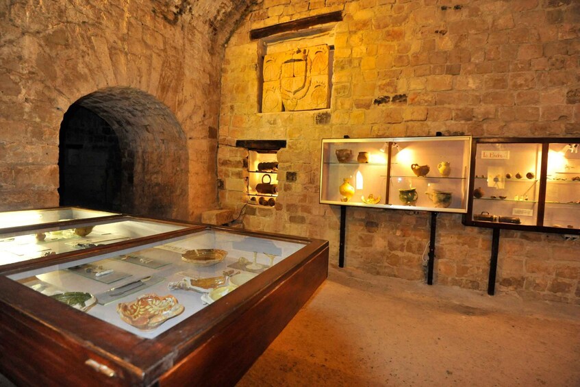 An interior with stone walls, a display case with artifacts, and a coat of arms on the wall. 2