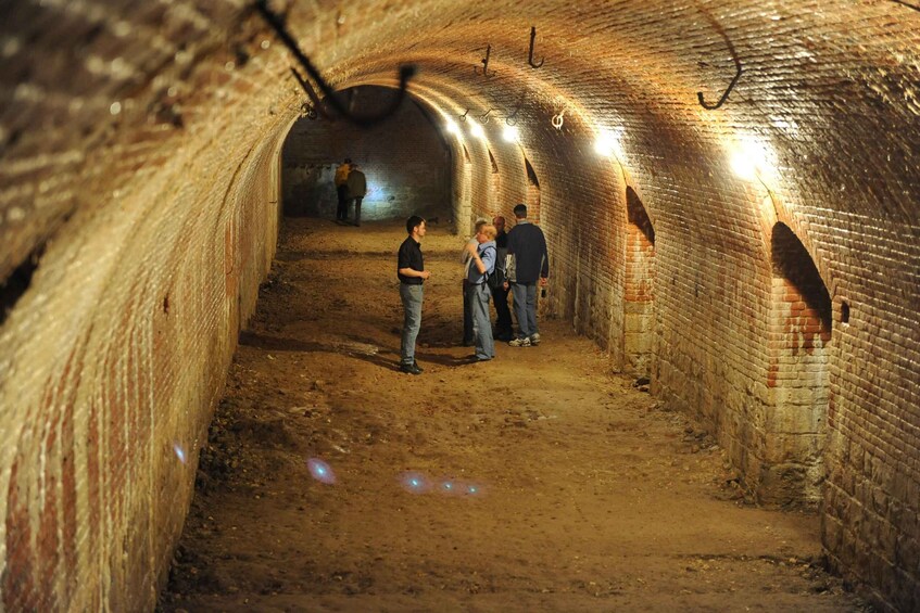 A tunnel with brick walls and a dirt floor, with people walking inside. 5