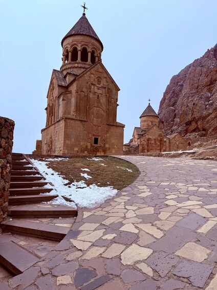A stone church with a dome and cross, surrounded by rocky terrain and a paved path. 2