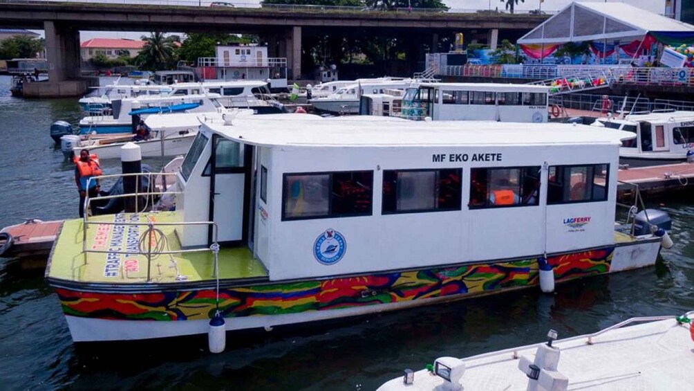 A white boat with colorful artwork on its side, docked at a marina with other boats and a bridge in the background. 3