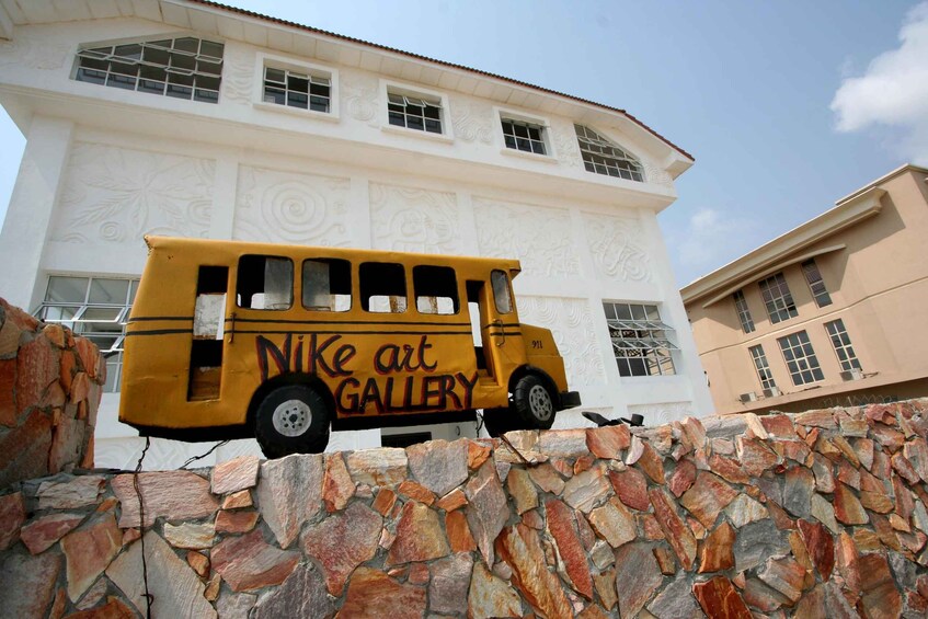 A yellow school bus parked in front of a white building with the words 'Nike art GALLERY' on its side. 4