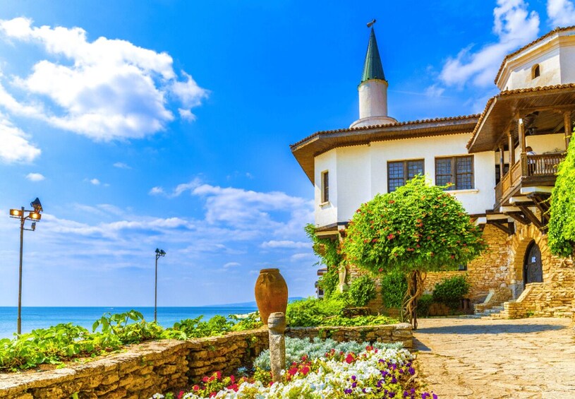 A coastal building with a green roof, a stone wall, and a garden with flowers. 1