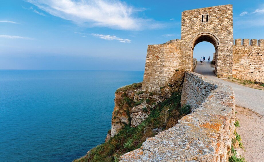 A stone bridge arching over a coastal road, leading to a historic stone wall. 3