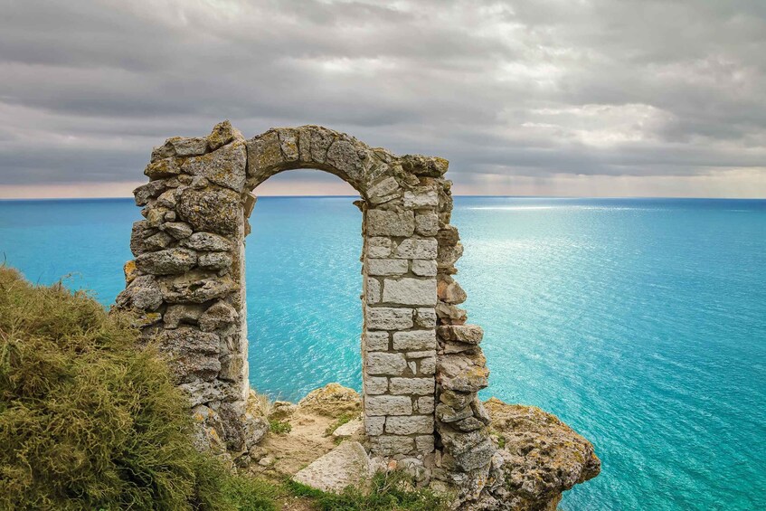 A stone archway leading to a coastal area with clear blue waters. 5