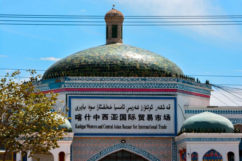 A mosque with a large green dome and a sign in English and another language. 2
