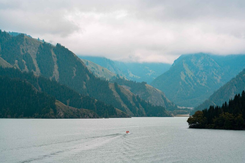 A lake surrounded by mountains, a boat on the water, and a cloudy sky. 1