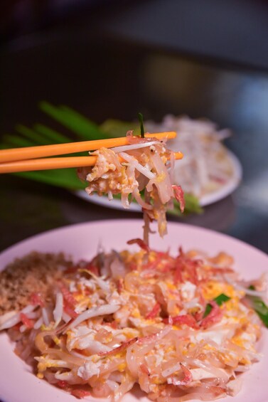 A plate of stir-fried noodles with vegetables and shrimp, being lifted by chopsticks. 3