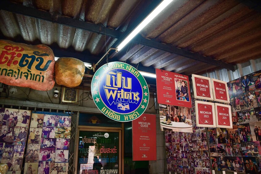 A shop with a large blue sign, various posters, and a corrugated metal roof. 2