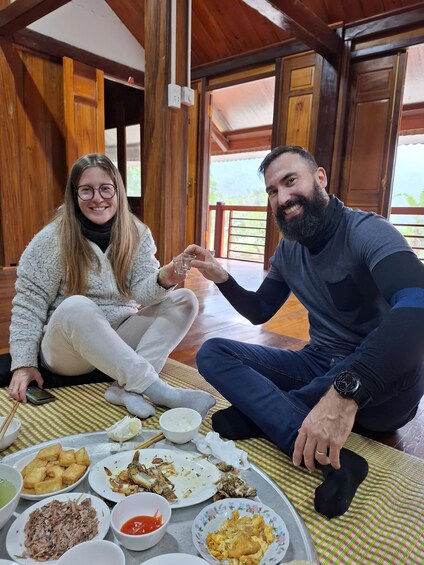 Two people sitting on a checkered mat indoors with wooden walls and a balcony in the background. 3