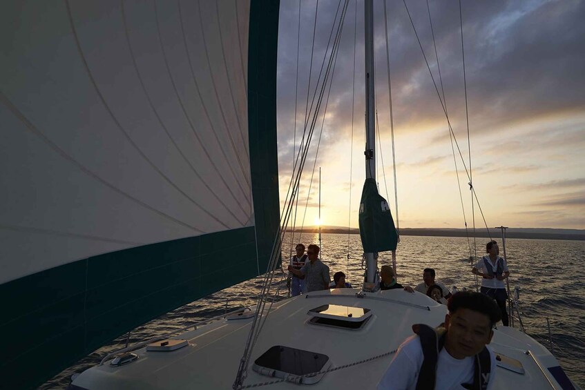 A sailboat with people on deck during sunset. 1
