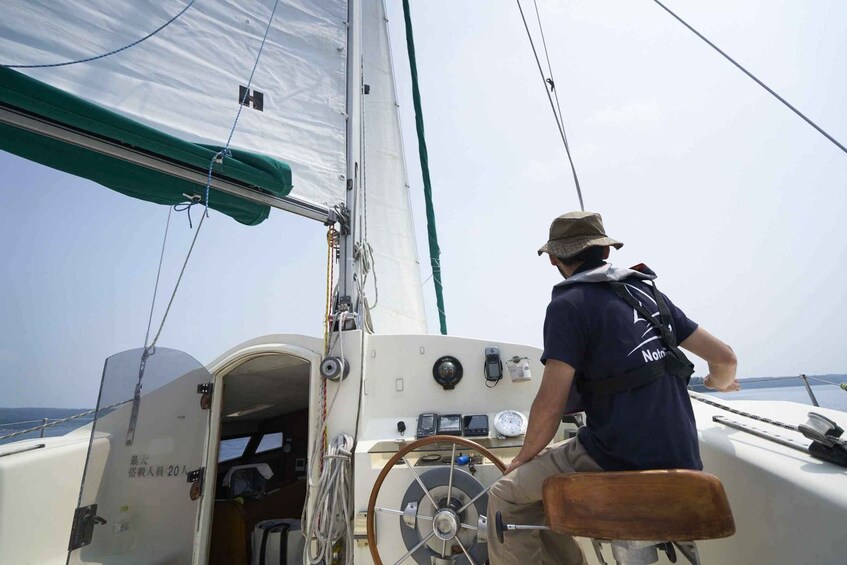A person steering a sailboat, with a steering wheel and various controls visible. 4