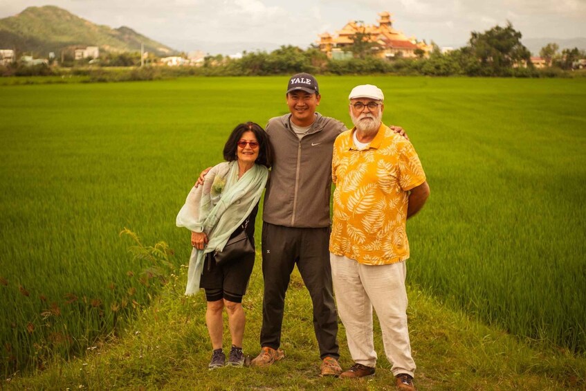 Three people standing in a green field with a building in the background. 1