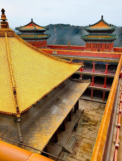 A traditional Chinese temple with golden roofs and red walls, set against a mountainous backdrop. 1