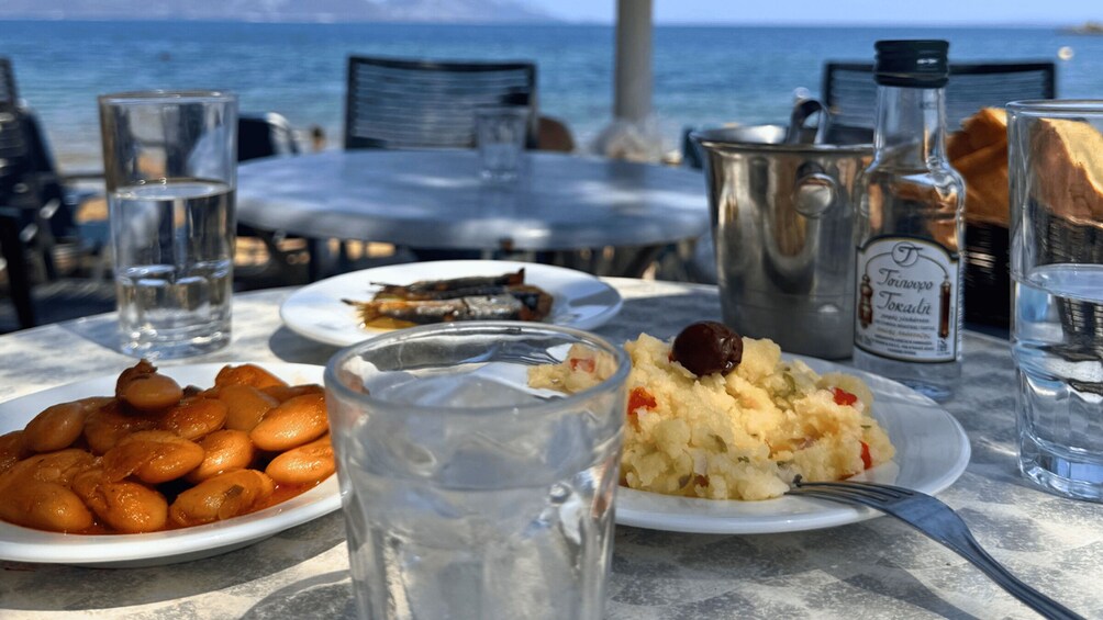 A table with plates of food, a bottle, and glasses of water at a seaside restaurant. 2