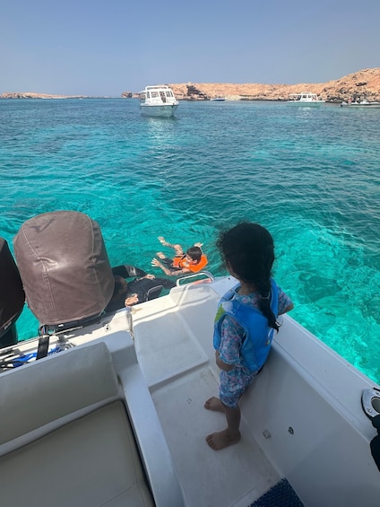 A child on a boat, looking at another boat with a person in the water. 3