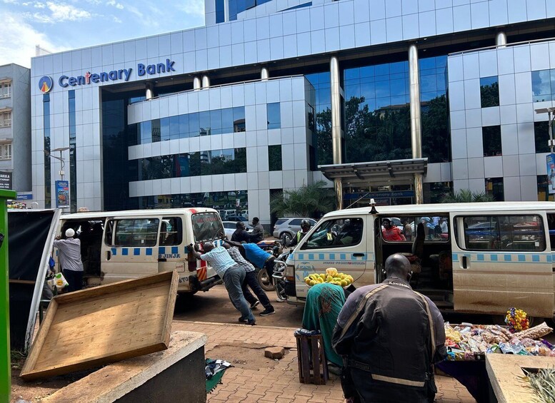 A busy street scene in front of a Centenary Bank building with several vans and people. 1