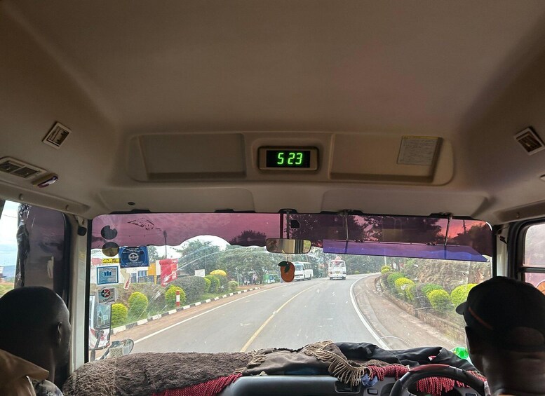 A bus interior with a digital clock displaying 5:23, a window view of a road with vehicles, and a person in the driver's seat. 2