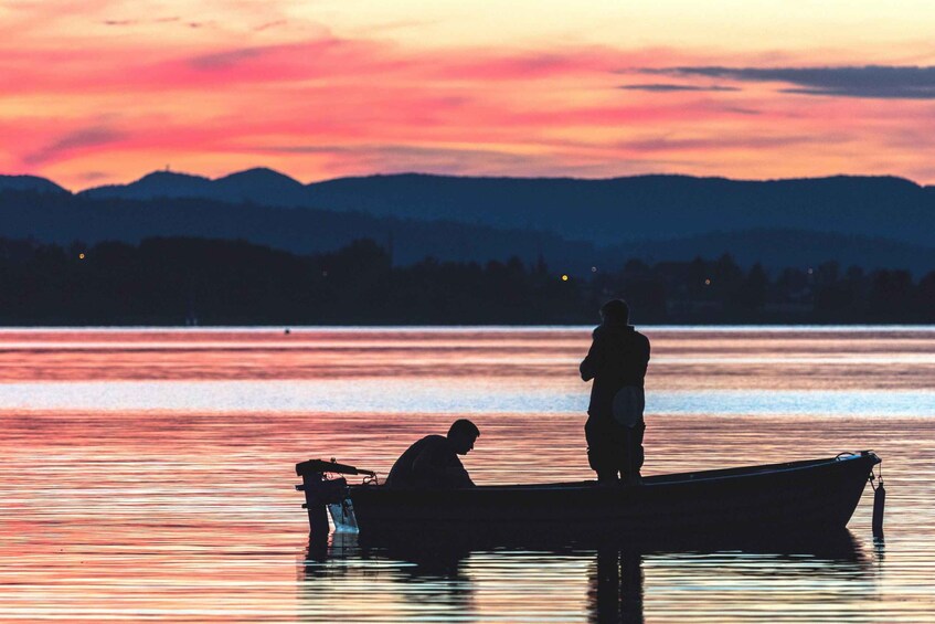 A sunset over a calm lake with two people on a boat. 1