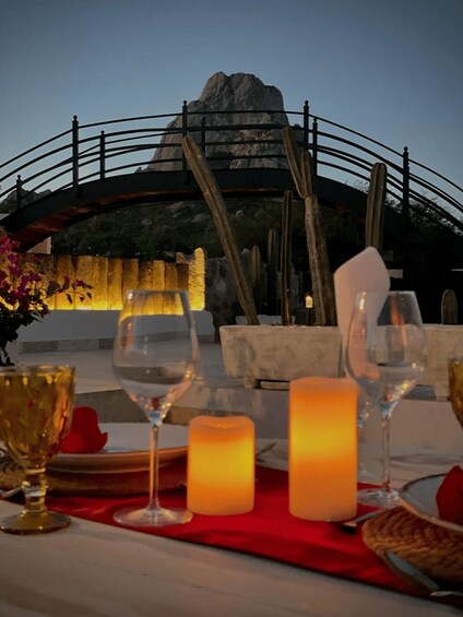 A table set for a meal with candles and wine glasses, overlooking a mountainous landscape. 1