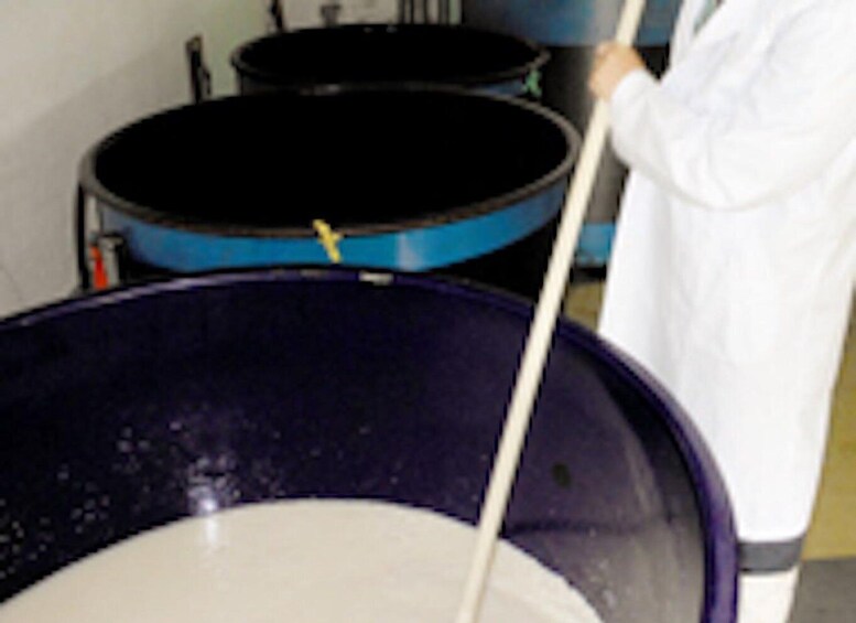 A person in a white lab coat stirring a large blue container. 4