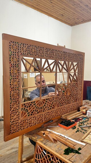 A person working on a wooden structure with a geometric pattern, surrounded by various woodworking tools and materials. 4