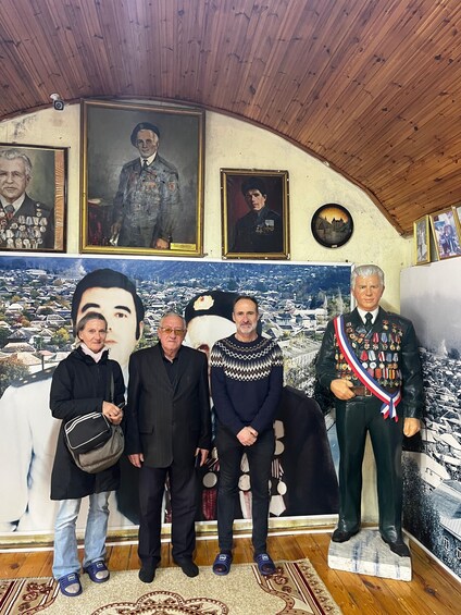 A group of people standing in front of a large mural with military portraits and a cityscape. 3