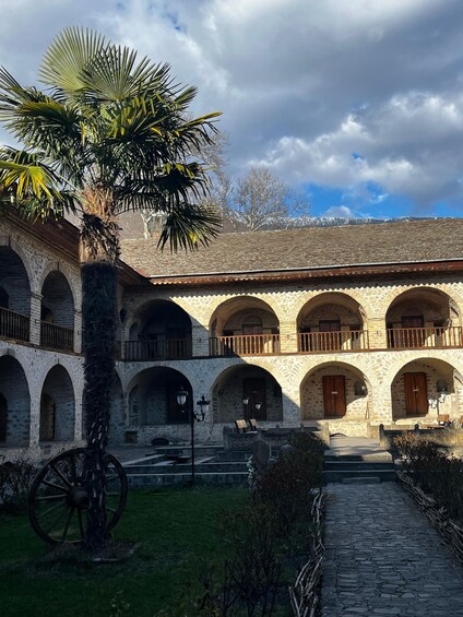 A courtyard with stone arches, a palm tree, and a vintage cart. 5