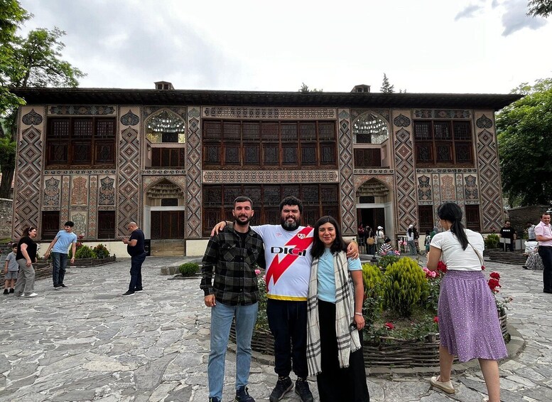 A group of people posing in front of a building with intricate tile work and arched windows. 2