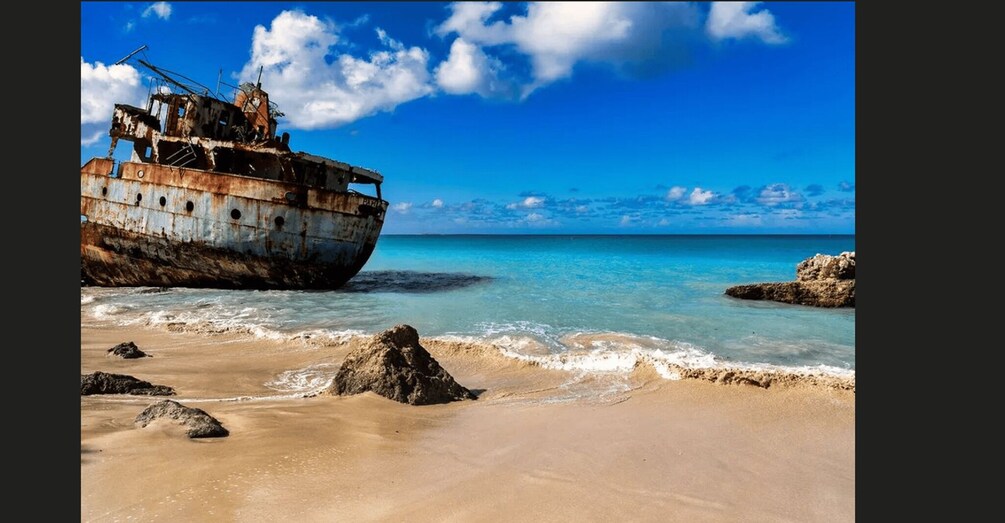 A sunlit beach with a rusted shipwreck and clear blue waters. 4