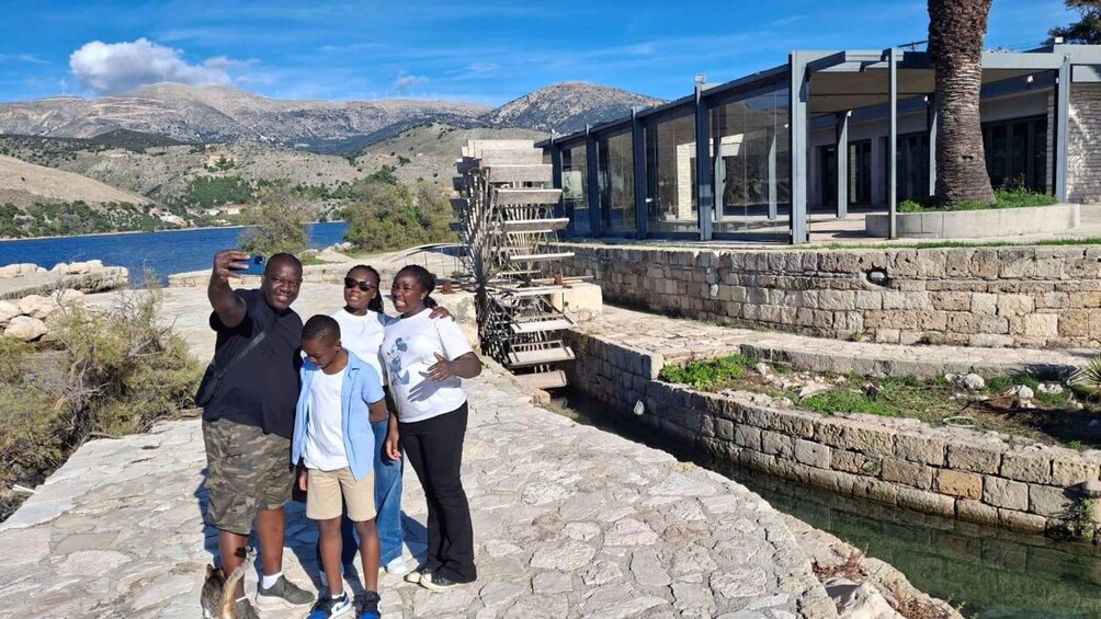 A family taking a selfie by a waterfront with a modern building and a mountainous backdrop. 2