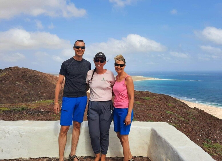 Three people standing on a cliff overlooking a beach with ocean waves. 1