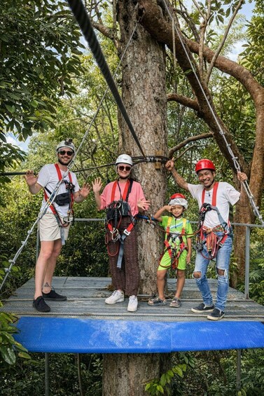 Four people on a tree platform with safety harnesses, surrounded by trees. 4