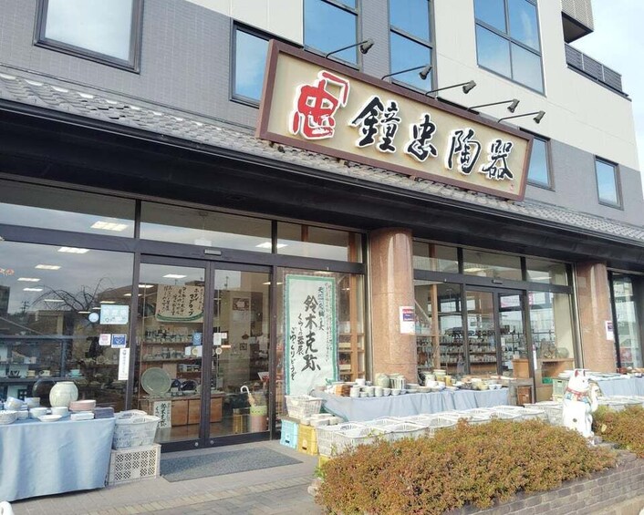 A storefront with a sign in Japanese characters, a display of ceramics outside, and a building with large windows. 2