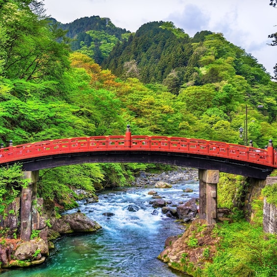 A red bridge over a flowing river surrounded by lush greenery and hills. 1