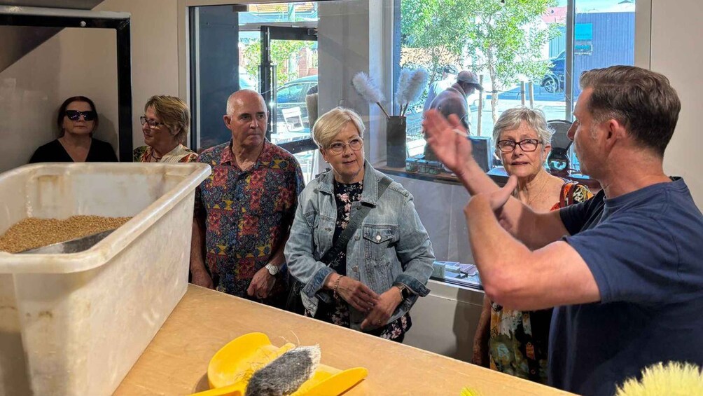 A group of people gathered around a table with a large container of grains and a yellow object on it. 3