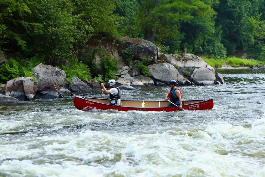Two people paddling a red canoe on a river surrounded by rocks and greenery. 5