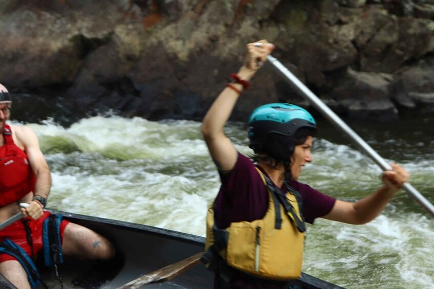 Two people in a kayak navigating a river with white water rapids. 4