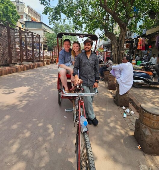 A person on a bicycle with a cart, a tree, and a street with shops and parked vehicles. 5