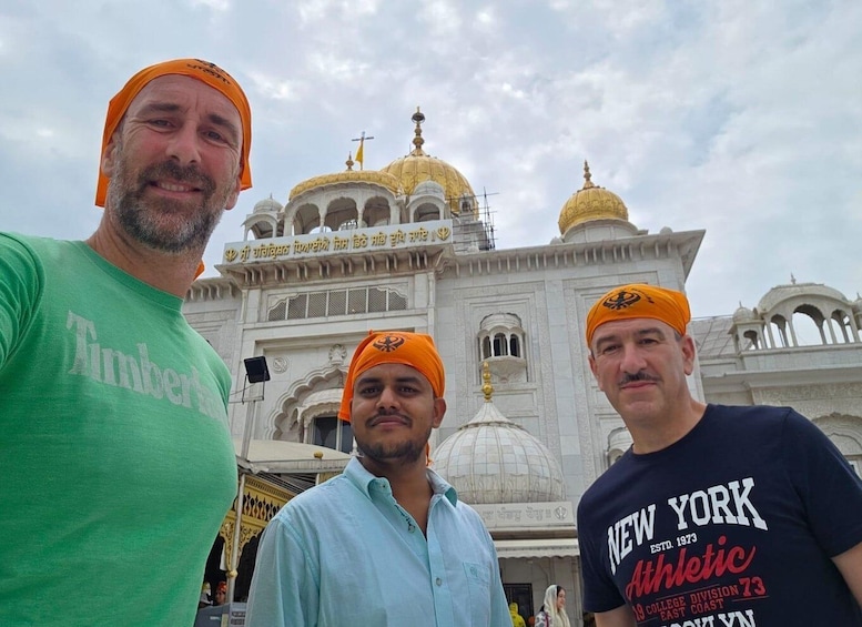 Three individuals in front of a large, ornate building with domes and intricate architecture. 1