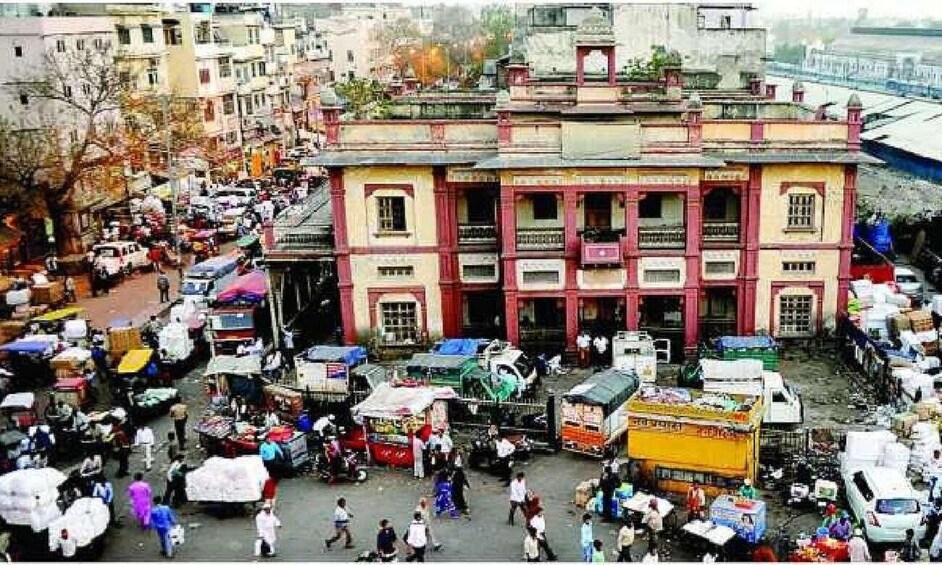 A busy street with a prominent building with balconies and a market area with various stalls and vehicles. 3