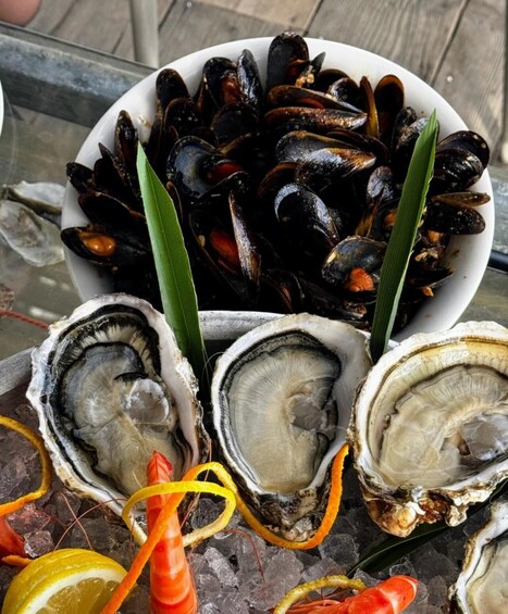 A bowl of mussels and oysters on a bed of ice with lemon slices and green leaves. 3