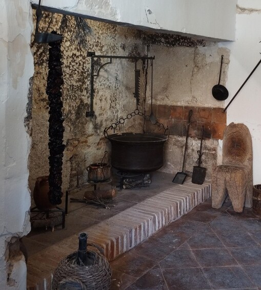A rustic kitchen with a large pot on a stove, a hanging pot rack, and various cooking utensils. 2