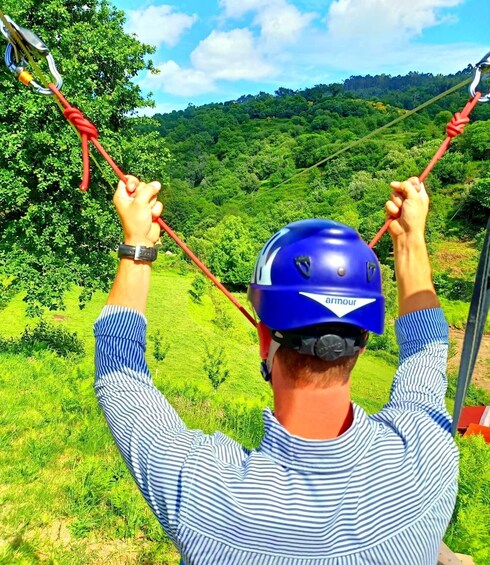 A person in a blue helmet and striped shirt holding onto a zip line. 3