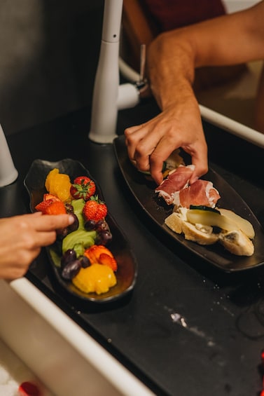 A person preparing a meal with a variety of fruits and vegetables on a black plate. 5