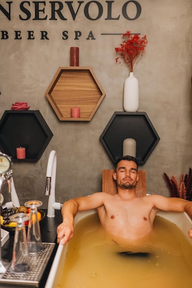 A man relaxing in a bathtub with a sign above reading 'SERVO BEER SPA'. 1