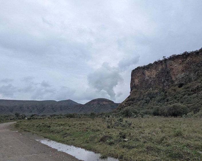 A road curving through a hilly landscape with a cliff on the right and a cloudy sky. 5