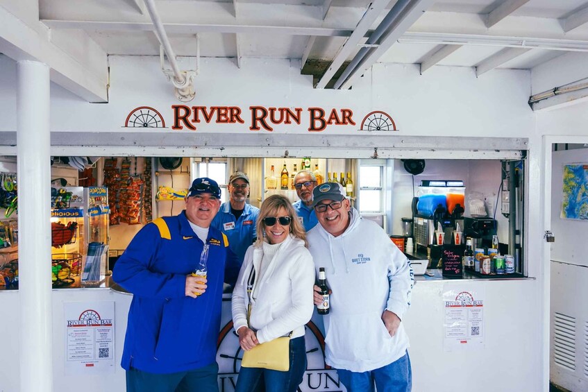 A group of people standing in front of a River Run Bar, with various beverages and snacks visible in the background. 3
