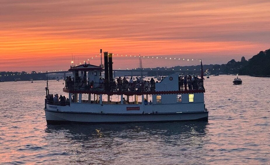 A riverboat with passengers, docked at sunset with city lights in the background. 4